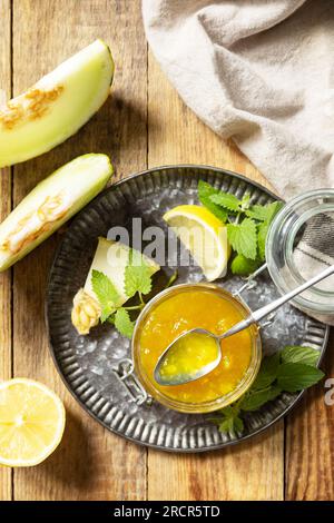 Süße Melone und Zitrusmarmelade oder Gelee in einem kleinen Glasgefäß mit frischen Melonenscheiben auf einem rustikalen Holztisch. Hausgemachtes Preserve. Blick von oben. Stockfoto