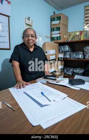 El Espino, La Libertad, El Salvador - 11 2022. Oktober: Ältere Lateinerin in schwarzem Hemd mit Brille steht am Schreibtisch eines Büros mit Papers an Stockfoto