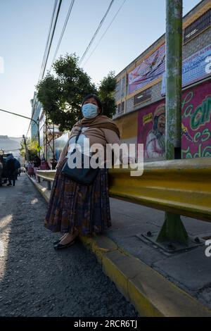 La Paz, La Paz, Bolivien - 12. August 2022: Eine indigene bolivianische Frau trägt eine Maske, während sie auf öffentliche Verkehrsmittel auf der Straße wartet Stockfoto