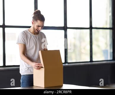 Aufgeregter Junger Mann Aus Dem Nahen Osten, Der Im Büro Einen Karton Öffnet Stockfoto
