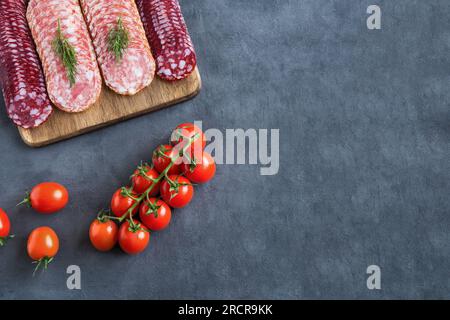 Das Servieren der Scheiben geräucherter Würste liegt auf einem Schneidebrett in mehreren Reihen auf einem Holzständer. In der Nähe gibt es Kirschtomaten. Die Zusammensetzung der flachen Verlegung beträgt Stockfoto