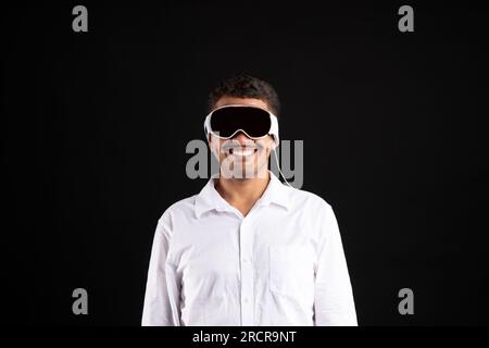 Ein fröhlicher brasilianischer Mann im Hemd trägt eine Vision Pro VR Brille und verwendet moderne Geräte auf schwarzem Studiohintergrund Stockfoto