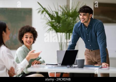 Fröhlicher arabischer Geschäftsmann kommuniziert mit Kollegen am Arbeitsplatz Stockfoto