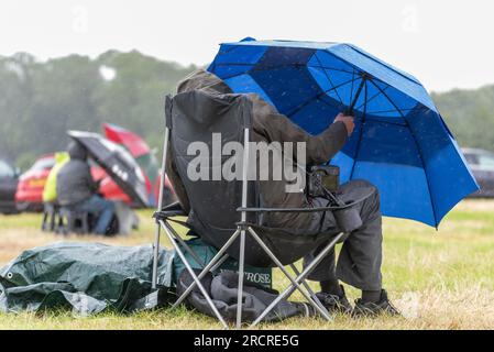 Fairford, Gloucestershire, Großbritannien. 16. Juli 2023. Flugbegeisterte, die die Royal International Air Tattoo Airshow anschauen, mussten sich während der Veranstaltung unter ein paar vorbeiziehenden Regenfällen verstecken Stockfoto