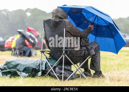 Fairford, Gloucestershire, Großbritannien. 16. Juli 2023. Flugbegeisterte, die die Royal International Air Tattoo Airshow anschauen, mussten sich während der Veranstaltung unter ein paar vorbeiziehenden Regenfällen verstecken Stockfoto