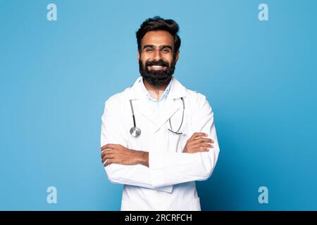 Der praktische Facharzt. Porträt eines fröhlichen indischen Arztes, der mit gefalteten Armen posiert und vor der Kamera lächelt Stockfoto