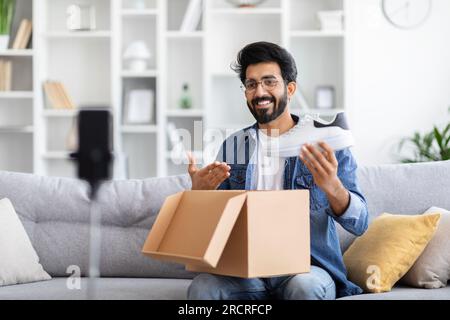 Lächelnder, glücklicher indischer Blogger, der ein Unboxing-Video für ein Paar Schuhe aufnimmt Stockfoto