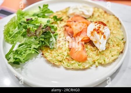 Zucchini-Pfannkuchen mit Avocado, Käsesahne, Lachs und Ei. Gesundes Frühstück, Eiweiß. Restaurant-Gericht. Frühstück im Café an einem sonnigen Morgen Stockfoto