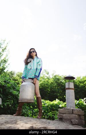 Junge, modische Bauernfrau, die vor der Kamera posiert, während sie die Milchdose hält Stockfoto