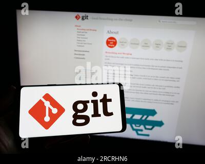 Person, die ein Smartphone mit dem Logo des verteilten Versionskontrollsystems Git auf dem Bildschirm vor der Website hält. Konzentrieren Sie sich auf das Display des Telefons. Stockfoto