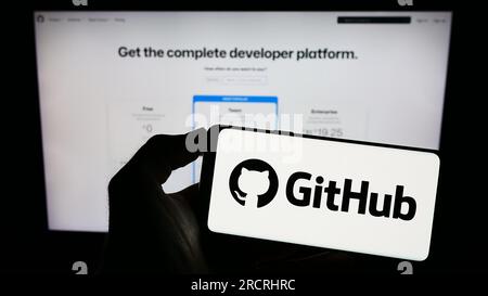 Person, die ein Mobiltelefon mit dem Logo des US-Softwareentwicklungsunternehmens GitHub Inc. Auf dem Bildschirm vor der Unternehmenswebseite hält. Konzentrieren Sie sich auf das Display des Telefons. Stockfoto
