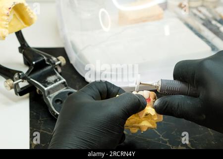 Nahaufnahme der Prothesenherstellung. Zahntechniker, der an der Prothese arbeitet, falsche Zähne. Zahnprothesenpolitur. Die zahnärztliche Prothesenarbeit. Stockfoto