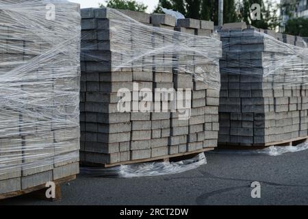 Klinkerplatten werden gestapelt: Stapel von Baustoffen auf der Straße sind für den Bau des Gehwegs bereit. Grauer Ziegel für den Bürgersteig. Stockfoto