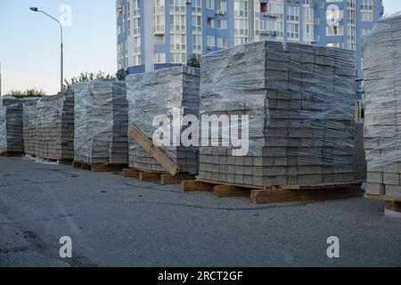 Auf der Straße gestapelte gepackte Straßenplatten: Stapel von Baumaterialien auf der Straße sind bereit für den Bau des Bürgersteigs. Grauer Ziegel für den Bürgersteig. Stockfoto