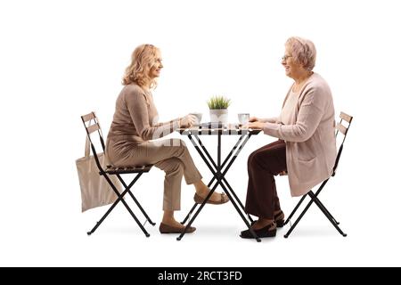 Ältere und jüngere Frau, die an einem Tisch sitzt und eine Tasse Kaffee trinkt, isoliert auf weißem Hintergrund Stockfoto