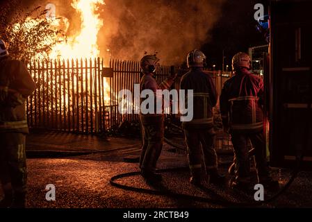 In der elften Nacht sahen Feuerwehrleute vor einem kleinen Lagerfeuer in der Nähe von Sandy Row. Um die Schlacht von Boyne zu feiern, werden Lagerfeuer in verschiedenen protestantischen Vierteln in Belfast gebaut, und Straßen und Häuser sind mit Union Jacks geschmückt. Die Lagerfeuer werden in der Nacht vor den Paraden zum 12. Juli angezündet. Stockfoto