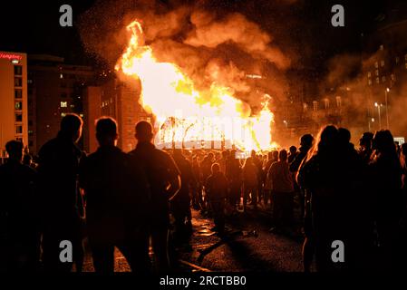 Belfast, Großbritannien. 14. Juli 2023. Protestanten und Loyalisten versammeln sich in der Sandy Row, um die 11. Nacht zu feiern, während sie ein großes Lagerfeuer in Flammen beobachten. Um die Schlacht von Boyne zu feiern, werden Lagerfeuer in verschiedenen protestantischen Vierteln in Belfast gebaut, und Straßen und Häuser sind mit Union Jacks geschmückt. Die Lagerfeuer werden in der Nacht vor den Paraden zum 12. Juli angezündet. (Foto: Natalia Campos/SOPA Images/Sipa USA) Guthaben: SIPA USA/Alamy Live News Stockfoto