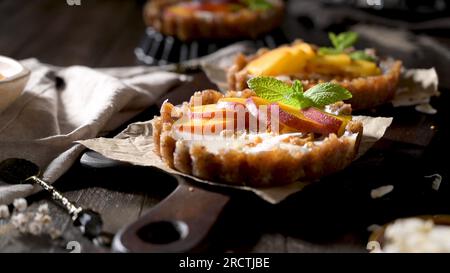 Vegane Pfirsichtörtchen mit geriebener Kokosnuss und knusprigen Erdnüssen. Obstkuchen. Dattel, Walnuss-, Mandel- und Haselnussbasis. Stockfoto