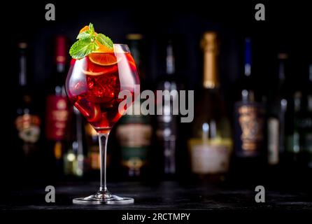 Rotes Sangria-Sommergetränk mit spanischem Rotwein, Pfirsich, Pflaume, Orange, Limette und Eis. Schwarzer Bartheke-Hintergrund, Stahlbarren und Flaschen Stockfoto