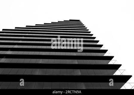 Schwarz-weiß, Low-Angel-Blick auf minimalistische moderne Wolkenkratzer mit horizontalem Glasgeländer vor dem gesamten Gebäude Stockfoto