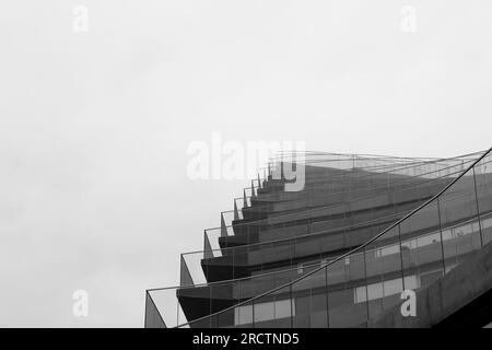 Schwarz-weiß, Low-Angel-Blick auf minimalistische moderne Wolkenkratzer mit horizontalem Glasgeländer vor dem gesamten Gebäude Stockfoto