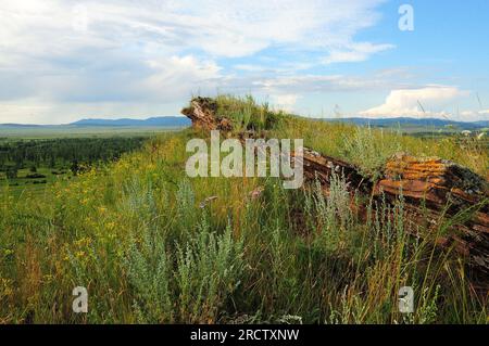 Eine mehrschichtige Felsformation aus rotem Sandstein auf einem hohen Grashügel mit Blick auf ein malerisches Tal an einem sonnigen Sommertag. Die Truhen der Bergkette, Khak Stockfoto