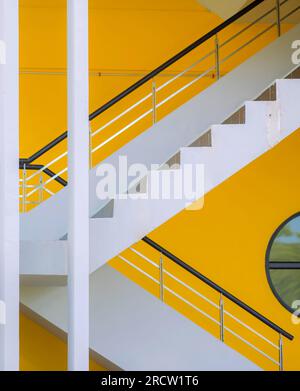 Seitenansicht einer modernen weißen Treppe mit schwarzen Balustraden und gelb bemalten Wänden. Stockfoto