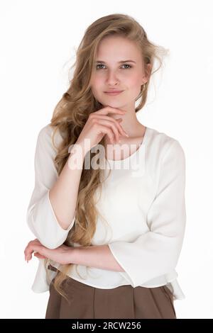 Porträt einer Weißen jungen Frau von 21 Jahren, die in die Kamera schaut. Wunderschöne blonde Frau mit langen Haaren, gekleidet in weißer Bluse und brauner Hose Stockfoto