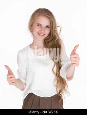 Eine glückselige blonde Frau, die mit beiden Händen Daumen nach oben zeigt und in die Kamera schaut. Verspielte, weiße, junge Erwachsene Frau, gut gekleidet in weißer Bluse Stockfoto