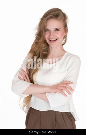 Selbstbewusste junge Geschäftsfrau, die lächelt und in die Kamera schaut. Gut gekleidete weiße Frau in weißer Bluse und brauner Hose kreuzte die Arme Stockfoto
