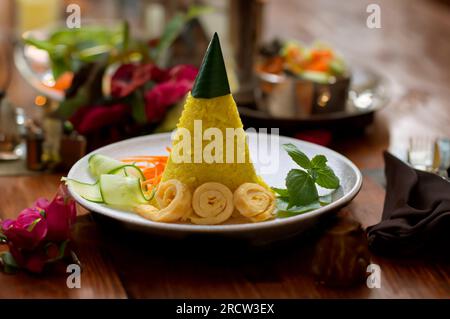 Nasi Tumpeng Mini. Gelber Reis in Kegelform. Ein festliches indonesisches Reisgericht mit Beilagen. Stockfoto