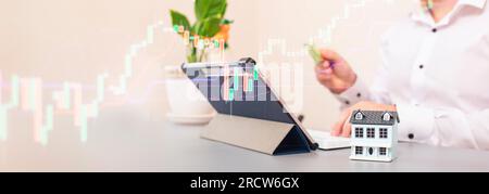 Das Konzept des Kaufs und Verkaufs von Immobilien. Ein Mann mit einem Modell eines Hauses im Hintergrund des Forex Stockfoto