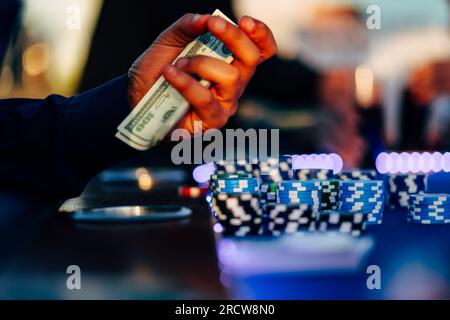 Männlicher Spieler sitzt neben Roulette mit Bargeld in der Hand und es liegen Casino-Chips auf dem Tisch. Stockfoto