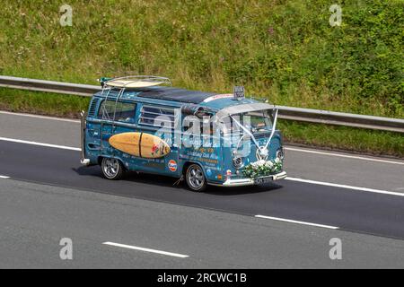 Warrens Vintage VW. 1973 70s 70er Blue Custom VW Volkswagen Motor Caravan LCV Benzinmotor 1584 cm3 Ein kurioser Hochzeitswagen mit Hippie-Dekoration, weißen Bändern und Surfbrett, der mit hoher Geschwindigkeit auf der Autobahn M6 in Greater Manchester, Großbritannien, fährt Stockfoto