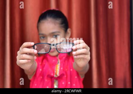 Ein indisches kleines hübsches Mädchen, das mit ihrer Brille in verschiedenen Posen in rotem Kleid rumfummelt. Stockfoto