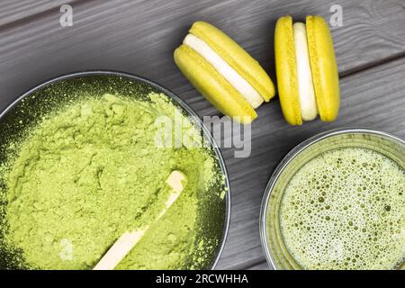 Zwei Makronen und Vatcha-Tee in der Schüssel. Grünes Matcha-Teepulver in schwarzer Schüssel. Flach verlegt. Dunkler Holzhintergrund Stockfoto