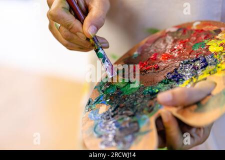 Mittelteil einer birassischen Frau mit Pinsel und Farbpalette im Heimstudio Stockfoto