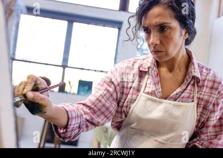 Birassische Frau, die Schürzenmalerei auf Staffelei trägt, mit Pinsel im Heimstudio Stockfoto