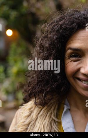 Porträt einer glücklichen, birassischen Frau mit dunklen, lockigen Haaren, die im Garten lächeln Stockfoto