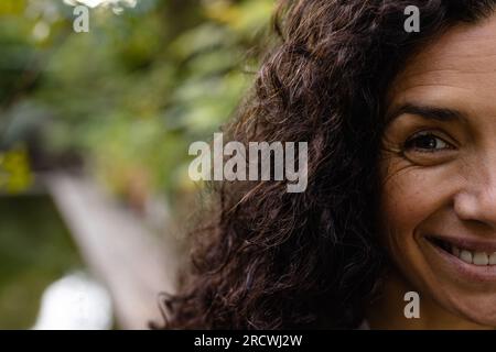 Porträt einer glücklichen, birassischen Frau mit dunklen, lockigen Haaren, die im Garten lächeln, Kopierraum Stockfoto