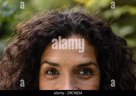 Porträt einer glücklichen, birassischen Frau mit dunklen, lockigen Haaren, die im Garten lächeln Stockfoto