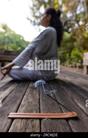 Räucherstäbchen über einer birassischen Frau, die Yoga macht, auf der Terrasse im Garten meditiert Stockfoto