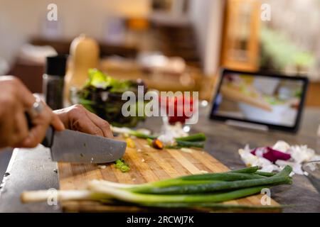 Mittelteil einer birassischen Frau, die eine Schürze trägt, das Essen kocht, Gemüse in der Küche hackt Stockfoto