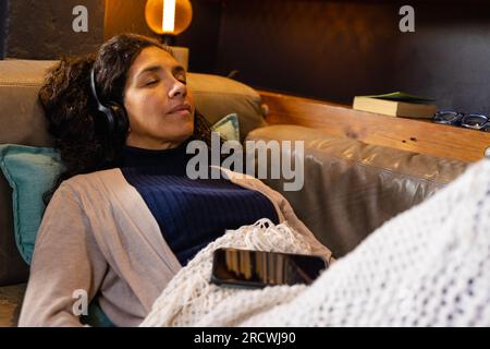 Birassische Frau, die auf dem Sofa liegt und im Wohnzimmer Kopfhörer trägt Stockfoto