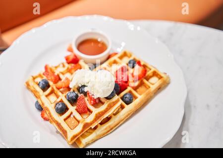 Klassische Wiener Waffeln mit Eis, Beeren und Ahornsirup. Frühstück im Café. Tisch im Restaurant. Stockfoto