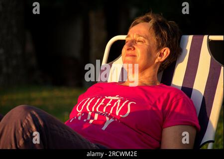Porträt einer Seniorin, die bei Sonnenuntergang auf einem Liegestuhl sitzt Stockfoto