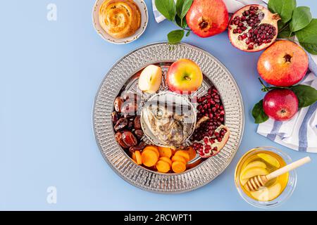 Ein Gericht mit Neujahrsgeschenk für den Neujahrsfeiertag Rosh Hashanah. Granatäpfel, Honig, Datteln, Apfelscheiben und Karotten. Blauer Hintergrund. Stockfoto