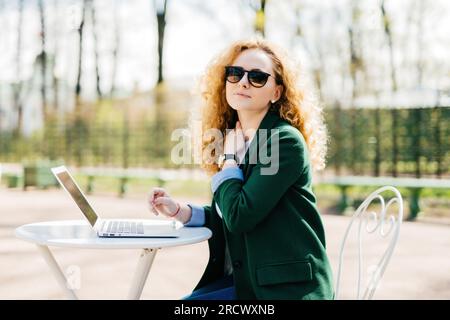 Erschöpfter Freiberufler, trendige Kleidung, flauschige blonde Haare. Müde, in der Natur isoliert, Laptop, Hand am Hals. Stockfoto