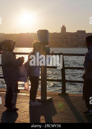 Sommersonnenuntergang über dem Bosporus von Uskudar auf der asiatischen Seite von Istanbul, Türkei. Eine Familie wird gerade ein Fernglas benutzen, um die Aussicht zu genießen. Stockfoto