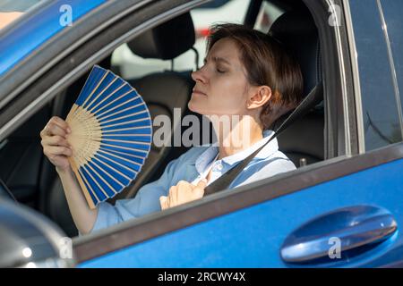 Erschöpfte Frau mittleren Alters fährt Autowellen blauer Fan leidet an Stau im Verkehr. Stockfoto